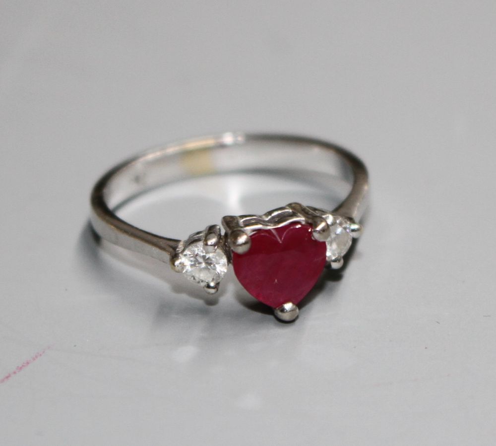 A modern 750 white metal, claw set heart shaped ruby and two round cut diamond set dress ring,